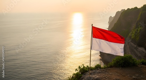 The Indonesian flag waves proudly on a cliff overlooking the ocean during a beautiful sunset.