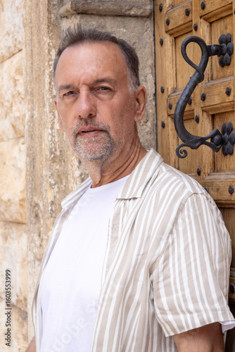 Senior man in summer outfit standing by rustic wooden door.