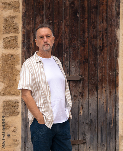 Senior man in summer outfit standing by rustic wooden door.