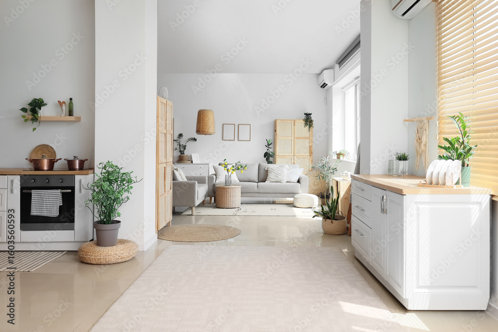Fototapeta premium White counters with dishware,comfortable sofa and houseplants in interior of room