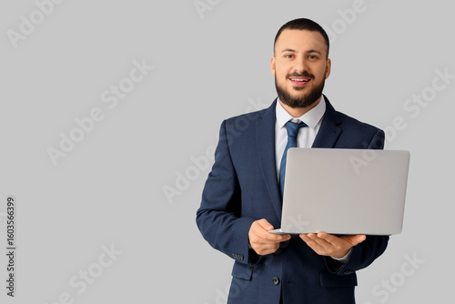 Handsome businessman with laptop on light background