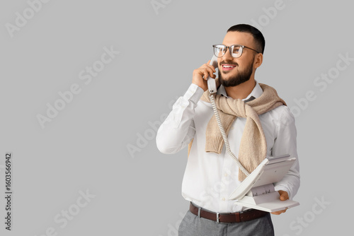 Male teacher talking by telephone on light background