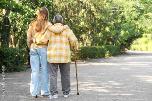 Senior woman with stick and caregiver hugging in park, back view