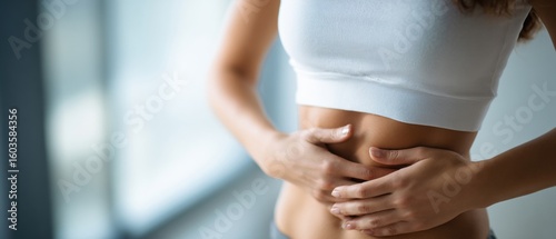 Woman in a white sports top holding her stomach, possibly indicating discomfort or focusing on abdominal area.