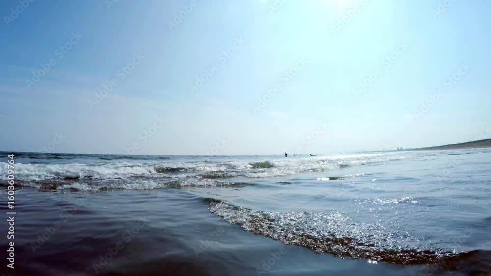 Gentle ocean waves rolling towards the shore under a clear blue sky