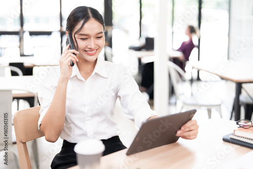 Charming woman using smartphone while working with digital tablet, sits in co-workspace.