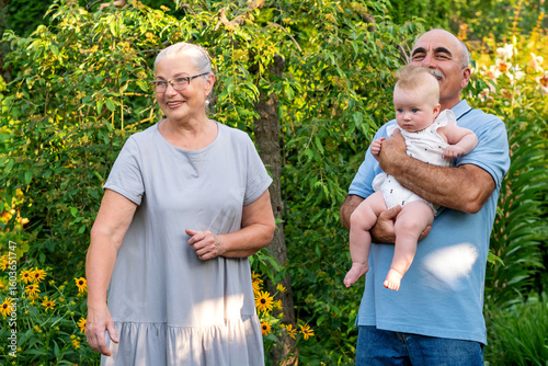 Grandparents warmly hold their baby and toddler outdoors in a lush garden, capturing joyful intergenerational bonding and family togetherness