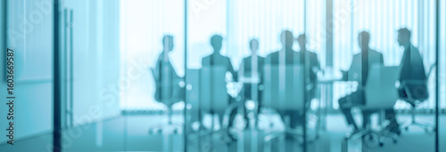 Blurred business people in suits sit at a table in modern office.