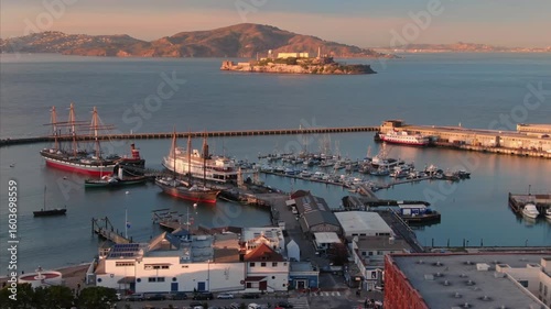 San Francisco Maritime National Historical Park, USA. Tourists visit historic ships at Hyde Street Pier, with Alcatraz Island in the background, to learn about maritime history.