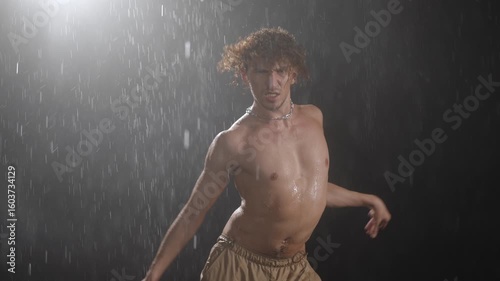 In a studio setting, a captivating male dancer performs with striking expressiveness amidst rainlike conditions