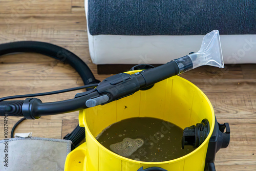 Obraz na plátně Carpet extractor with dirty water after upholstery cleaning, placed on wooden floor next to a sofa
