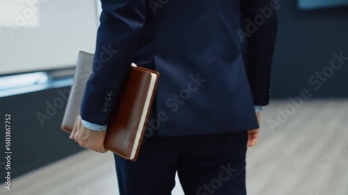A man walks into a meeting room with a leather notebook in hand, and the camera follows his hand movements
