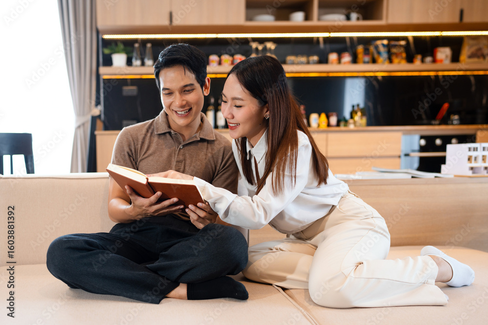 Young couple man and woman asian husband and wife in a relationship reading book hold books on the sofa couch at home in the apartment reading leisure bonding family concept . copy space. Young couple man and woman asian husband and wife in a relationship reading book hold books on the sofa couch at home in the apartment reading leisure bonding family concept . copy space.
