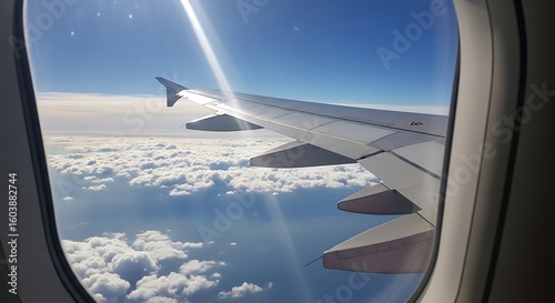 Airplane wing seen through the window during flight, with a view of clouds and the sky.