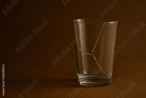 Cracked transparent glass cup on brown background with visible fracture lines