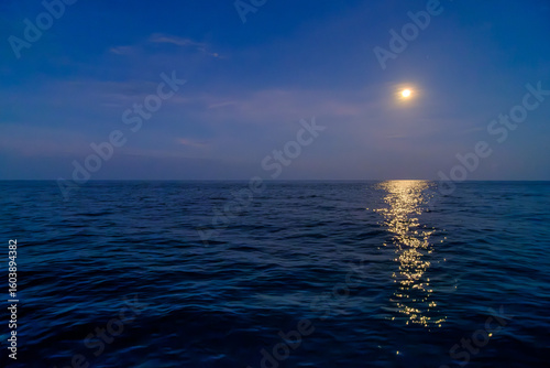 a yellow vivid bright full moon in the blue sky over the open sea
