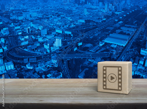 Play button with movie flat icon on wood block cube on wooden table over modern city tower, street, expressway and skyscraper, Business cinema online concept