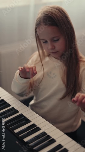A young girl sits and plays the piano in her home. She practices her piano skills and enjoys the music.