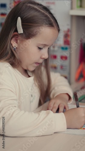 Young girl diligently drawing and coloring in a notebook at her desk. The scene evokes feelings of childhood, learning, and creativity.