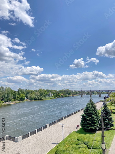 Landscape of the Dnipro embankment against the background of the Dnipro and the blue sky strewn with snow-white clouds.