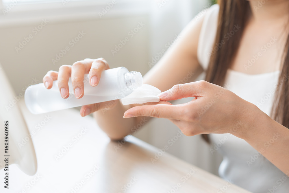 Naklejka premium Making beauty routine, attractive asian young woman hand holding cotton pad and bottle, female applying facial wipe on her face remover washing makeup, essence or lotion of skin care treatment at home