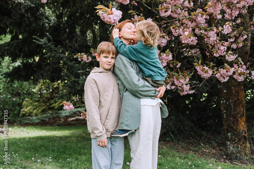Mother hugging sons under blooming tree in park enjoying closeness