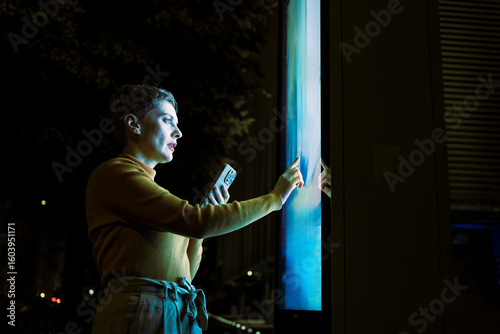 Woman using digital touch screen information display at night in city