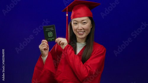 Woman in red graduation gown holding italian passport against blue background, showcasing academic achievement with identification highlight.