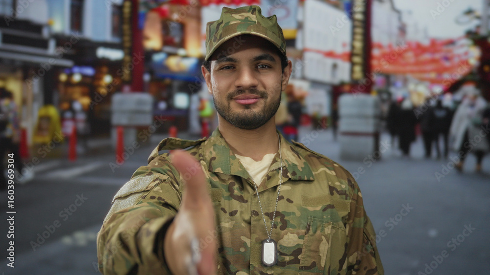 Fototapeta premium Man in camouflage uniform extending his right hand forward for a friendly handshake on a bustling street; trust.