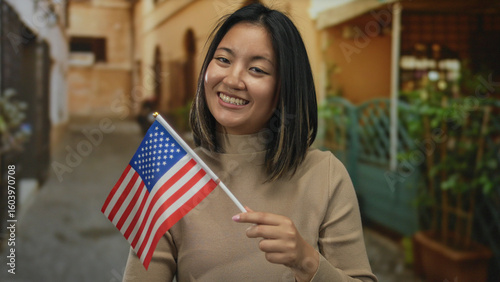 Fotografie Woman with asian descent holding american flag on city street smiling outdoors in usa, representing cultural diversity and patriotism in urban setting