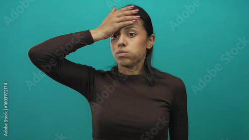 Hispanic woman in brown shirt gesturing emotionally against isolated green wall background.