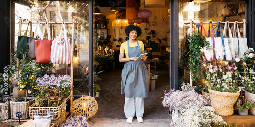 Florist owner holding digital tablet and smiling in front of her flower shop, small business and entrepreneurship concept