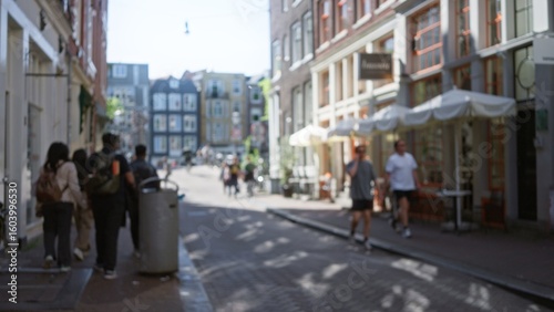 Fotografie Blurred city street in amsterdam with people walking in the foreground, showcasing a vibrant urban scene with colorful buildings and a bustling atmosphere, out of focus