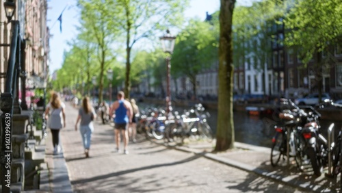Wallpaper Mural Blurred people walking alongside amsterdam canal with trees bicycles and historic buildings in the netherlands on a sunny day conveying a leisurely urban atmosphere. Torontodigital.ca
