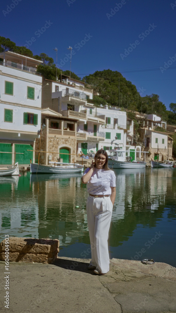 Fototapeta premium Woman standing at cala figuera port, mallorca, surrounded by boats and picturesque mediterranean buildings under a clear blue sky, portraying a tranquil and scenic atmosphere.