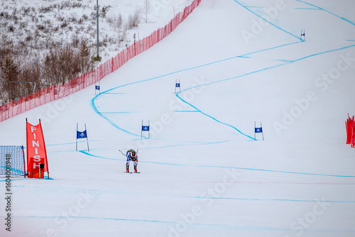 alpine ski athlete racing downhill on snowy ski slope passing finish line