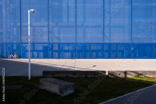 Blue glass facade with open paved plaza and bench, blending transparency and structure in an urban business district, excellent for generic urban context and design flexibility