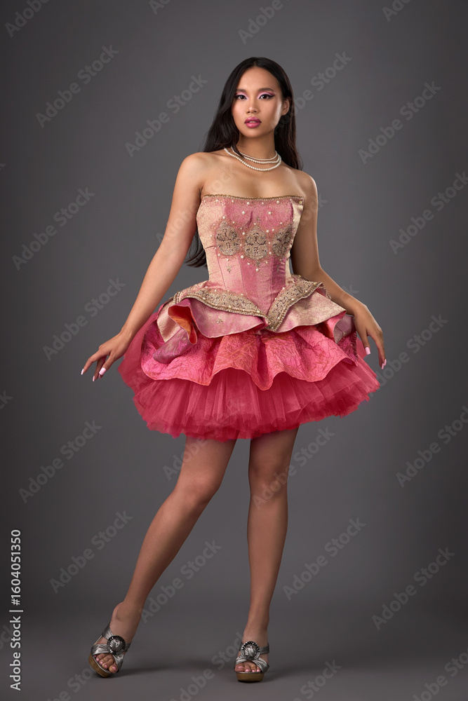 Naklejka premium Beautiful brunette Asian woman with exquisite makeup and manicure in a pink short dress on a gray background