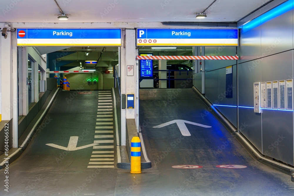 Obraz premium A well-lit parking garage entrance showcases clear directional arrows, barriers, and signage. Ideal for urban infrastructure, transportation, and vehicle management systems.