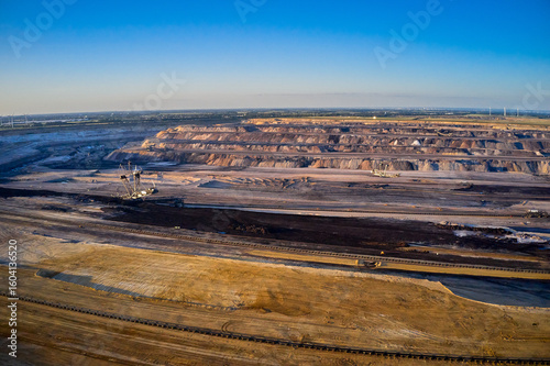 Aerial view of vast open-pit mine reveals stark contrasts of layered earth against the clear sky, a landscape transformed by industry, Lutzerath, Rhineland-Palatinate, Germany.