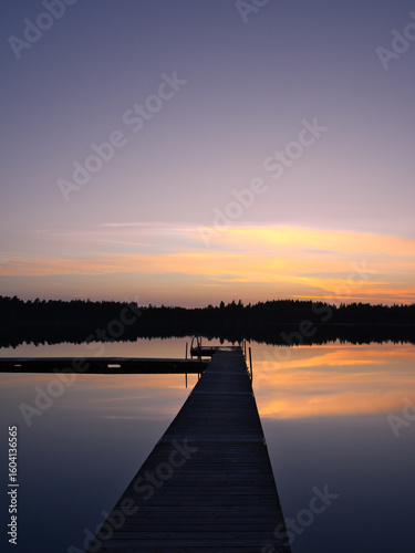 A wooden walkway in Sweden leads into a quiet lake at sunset. Scandinavia