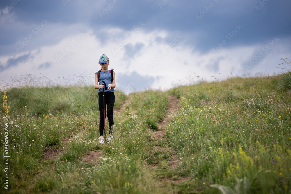 Obraz premium Young hiker pausing on a meadow path under cloudy sky