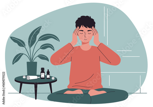 A person meditating in a lotus position with eyes closed, hands on temples, next to a table with essential oils and a potted plant.