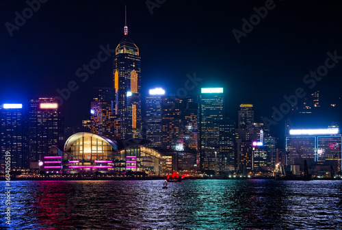 Hong Kong Skyline at Night with City Lights and Harbor Reflection. HK cityscape illuminates the night, with skyscrapers and convention center reflecting their colorful lights on Victoria Harbour.