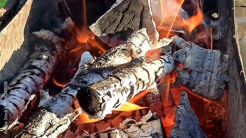 Close-up of burning firewood on barbecue outdoors in sunny weather.