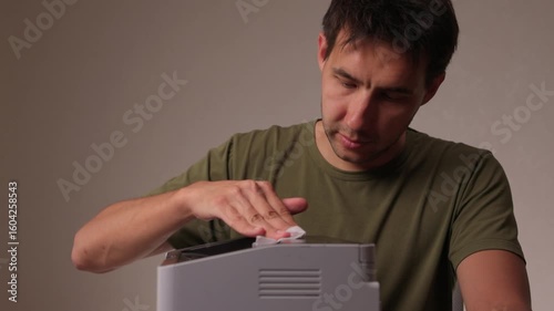A focused man cleaning a device with a cloth for proper maintenance and cleanliness