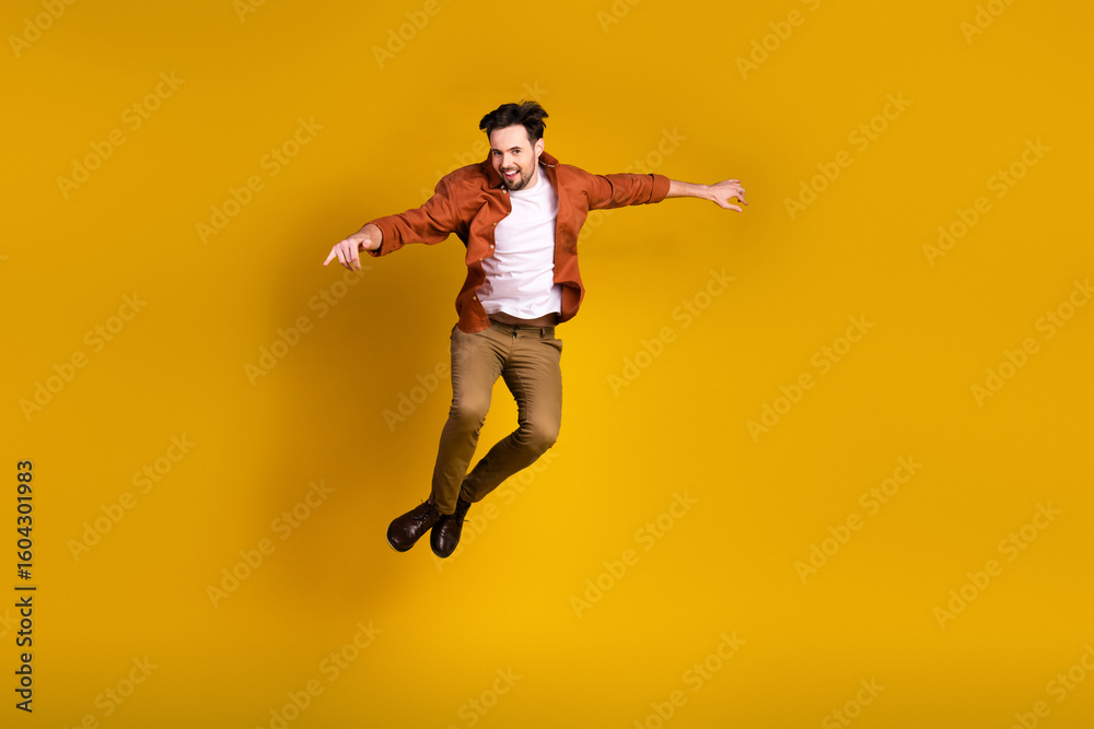 Obraz premium Dynamic portrait of a joyful young man in casual attire jumping energetically on a vibrant yellow backdrop