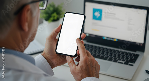 Male doctor holding cell phone in hands using blank white mockup screen technology ehealth mobile app for medical healthcare telemedicine ads, e telehealth online applications. Over shoulder view