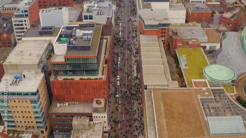 Aerial establishing shot tilts up revealing Belfast St. Patrick's parade streets and skyline