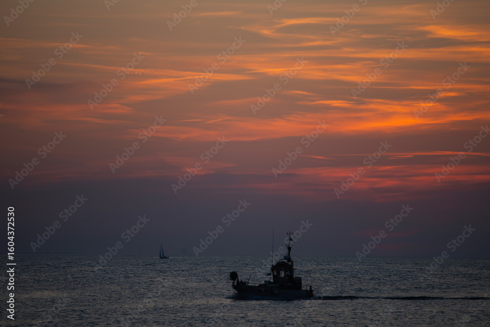 Obraz premium Boat silhoutted against the orange sky